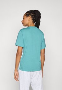 Turkos bomulls t-shirt med korta ärmar, rund halsringning och en avslappnad passform, tillsammans med ljusgråa sweatpants. Inga synliga mönster.