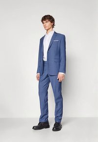 Zils uzvalks ar pieguļošu dizainu, vienrindu žakete, ar iegriezuma atloki, baltu krekliņu apakšā un melniem apaviem. Gluda tekstūra, moderna stila.