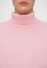 Roze coltrui gemaakt van zacht gebreide stof, met een aangesloten silhouet en ribbelstructuur rond de kraag en zoom.