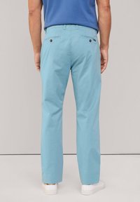 Chinos azul claro con corte recto, que cuentan con bolsillos traseros y detalles de botones, combinados con una camisa azul lisa y zapatos blancos.