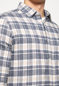 Kariertes Hemd aus weichem Stoff, mit Marineblau, Grau und Beige. Mit Knopfleiste am Kragen und vorderen Knöpfen; durchgehend im Karomuster.