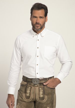 Weißes Langarmhemd mit Knöpfen und einer einzelnen Brusttasche, kontrastierenden braunen Knöpfen, kombiniert mit braunen bestickten Lederhosen und einem Gürtel.