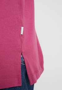 Rosa Baumwoll-T-Shirt mit seitlichem Schlitz und Saumdetails. Verfügt über ein kleines Etikett auf der linken Seite und mit darunter sichtbarem Denim-Stoff.