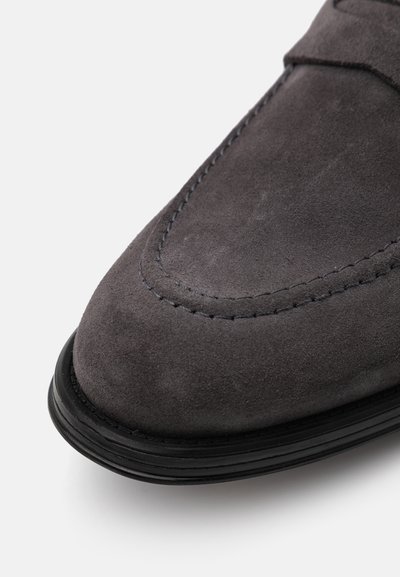 Grau Wildlederschuh mit runder Spitze, der sichtbare Nähte und eine schwarze Gummisohle aufweist. Die Textur wirkt weich und glatt.