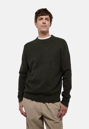 Pull en tricot vert foncé avec un col rond et des manches longues, associé à un pantalon en velours côtelé beige clair. Design de tissu simple et texturé.