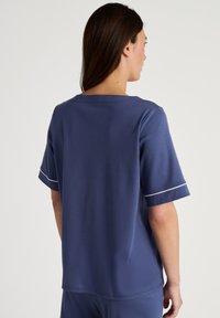 Marineblauwe T-shirt met korte mouwen en een brede ronde halslijn. Kenmerken zijn witte piping op de mouwen, gladde stof, relaxte pasvorm en minimale details.