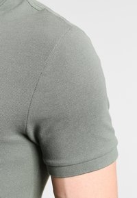 Polo à manches courtes en vert clair. Confectionné en tissu texturé avec un col et des poignets côtelés. Détails de coutures visibles sur l'épaule.