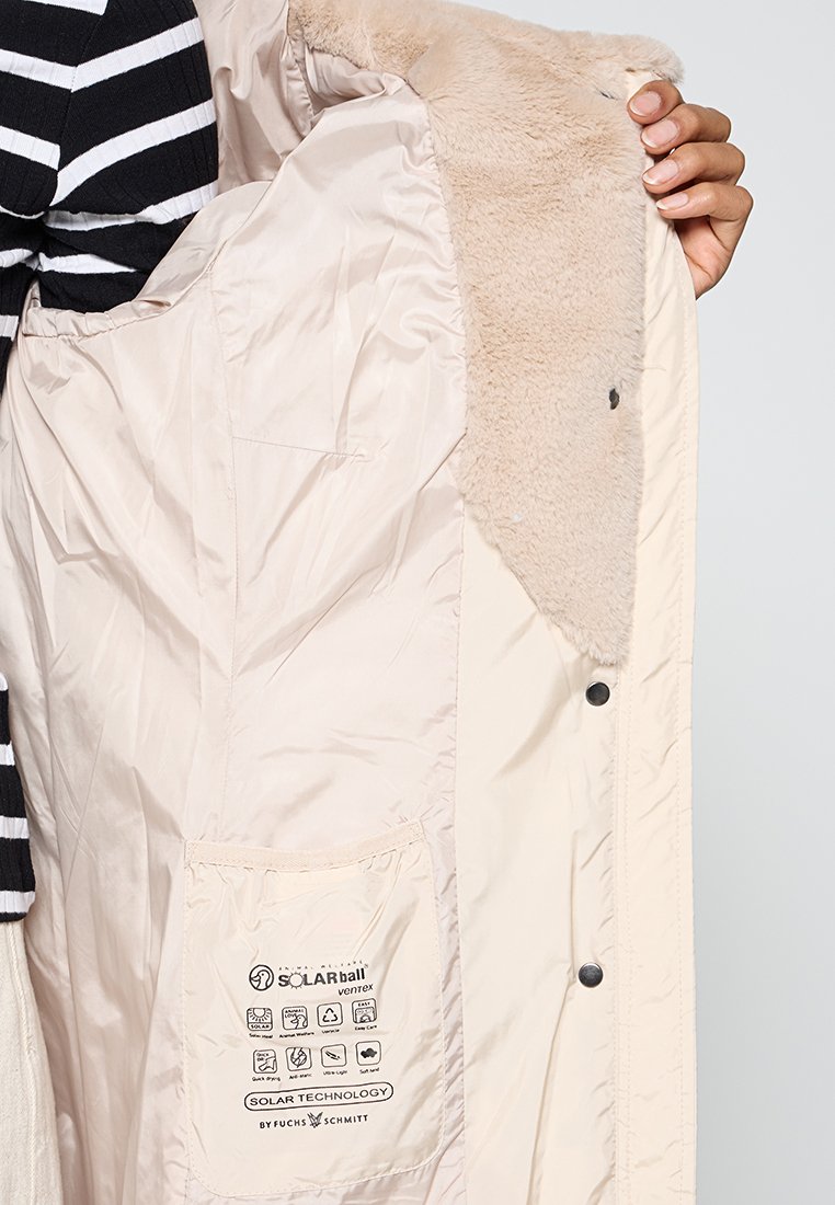 Beżowa kurtka z miękkim, sztucznym futrem w środku i gładkim materiałem zewnętrznym. Posiada kieszeń z instrukcją pielęgnacji oraz zapięcia na zatrzask.