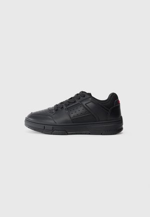 Czarny niski sneaker z perforowanym bocznym panelem, sznurowaniem, wyściełanym kołnierzem i teksturowaną podeszwą na jednolitym jasnym tle.