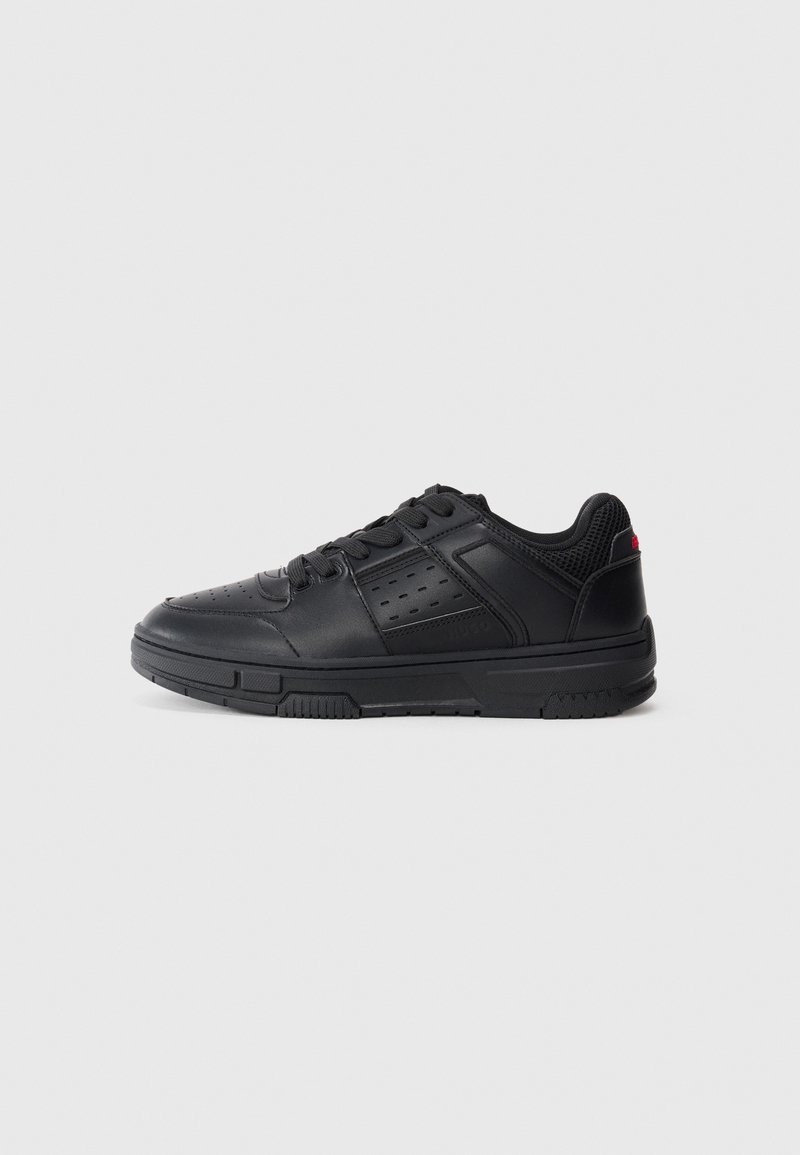 Baskets basses noires avec panneau latéral perforé, laçage, col rembourré et semelle texturée sur un fond clair uni.