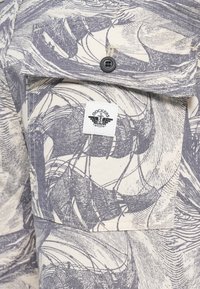 Short-sleeved, cotton shirt in cream with blue wave and ship print. Features a front pocket with a black button and a logo tag.