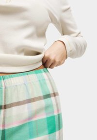 Lichtbeige geribbelde langemouwen top gecombineerd met lichte, geruite pyjamabroek in muntgroen, lichtbruin, roze en wit. Elastische tailleband zichtbaar.