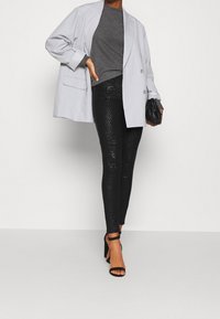 Light gray oversized blazer, dark gray fitted top, black textured leggings with a subtle snake print, and black heeled sandals.