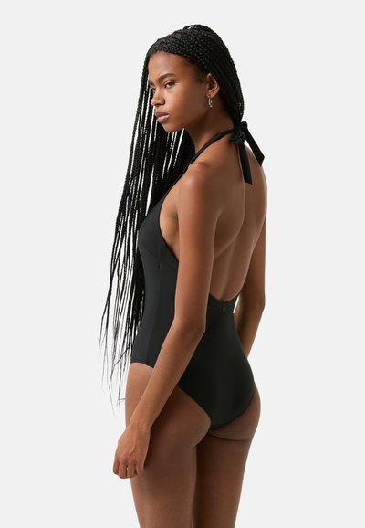 Black one-piece swimsuit with a low back, halter neck style, textured fabric, and a back tie detail, featuring a sleek, fitted silhouette.