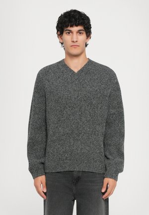Suéter gris de punto con un diseño de cuello en V, mangas largas y dobladillo acanalado. Hecho de una tela texturizada, que muestra un patrón sutil.