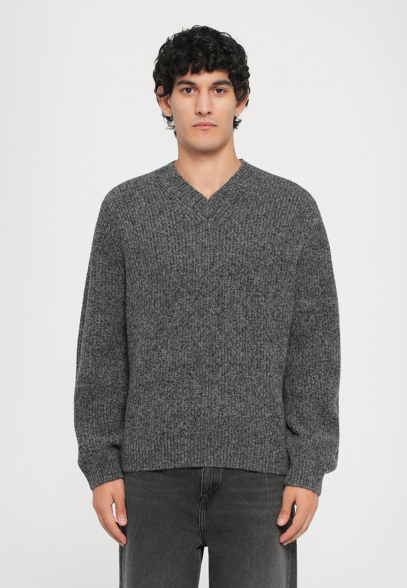 Gray knitted sweater with a v-neck design, long sleeves, and ribbed hem. Made of textured fabric, showcasing a subtle pattern.