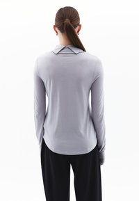 Langarmshirt van lichtgrijze stof, met een kraag, gebogen zoom en een aansluitende pasvorm. Het materiaal lijkt glad en licht van gewicht.