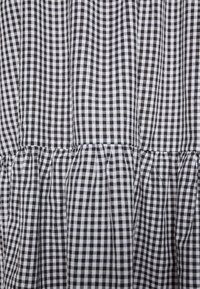 Zwart-wit ruitjesstof met een gestructureerd oppervlak en geplooide details. Het patroon bestaat uit kleine, afwisselende vierkantjes.