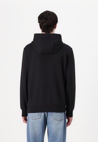 Felpa nera con un grande cappuccio, polsini a costine e orlo dritto. Mostrata da dietro, abbinata a jeans azzurri chiari.