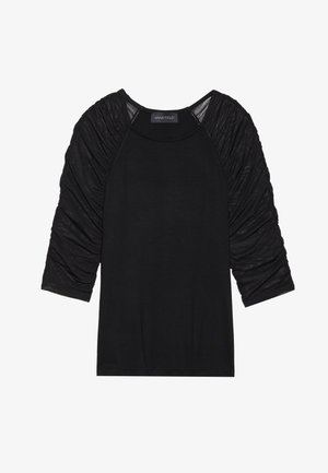 Svart topp med trekvartsärmar. Ärmarna har samlad, texturerad tyg. Kroppen är slät och figurnära. Etiketten säger "ANNA FIELD."