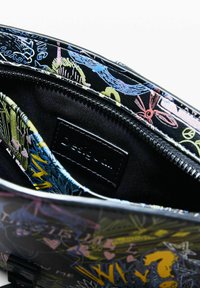 Interior din material textil negru al unei genți cu un model colorat, cu un fermoar vizibil și o etichetă a brandului cosută în interiorul buzunarului.