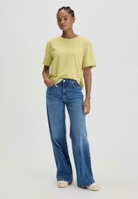 Lichtgele katoen t-shirt met korte mouwen, gecombineerd met hoogwaardige blauwe wijde jeans en beige sneakers. Glad textuur, casual pasvorm.