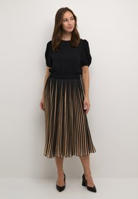 Juodas bliuskas su pūstomis rankovėmis, derinamas su gėlėta sijonu, kuriame pakaitomis juodos ir smėlio spalvos vertikalios juostos. Juodi aukšti kulniukai.