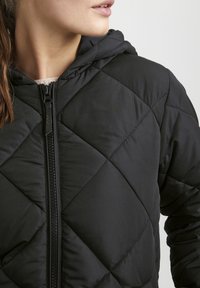 Svart vadderad jacka med huva, med en central dragkedja, diamantmönster och slät tygstruktur. Närbild på nackområdet.