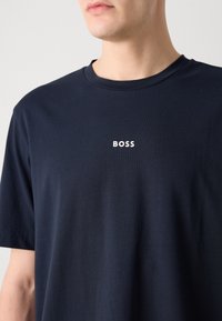 Homme portant un t-shirt bleu marine avec le mot "BOSS" imprimé en lettres blanches sur la poitrine.