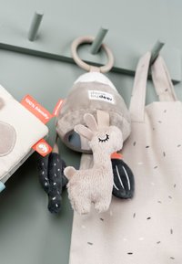 Pehmolelulama harmaassa ja beigen sävyissä, jossa kiinnityssilmukka. Pehmeät pinnat, kangastarrat ja vihreät kaktuselementit näkyvissä.