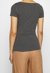Donkergrijze kortemouwen top met witte stippen, met een ronde halslijn en een getailleerde pasvorm. Gestructureerde stof met een zachte uitstraling.