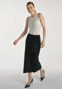 Czarna spódnica w kratę z paskiem do wiązania, zestawiona z dopasowanym białym topem ribbed. Strój uzupełniają czarne, szpiczaste szpilki oraz gładka faktura materiału.