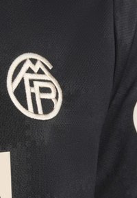 Zwarte stof met een gestructureerd oppervlak, voorzien van een geborduurd logo in lichtbeige. Het logo bevat berg- en letterontwerpen op de stof.