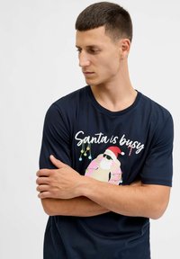 Marineblauwe katoenen t-shirt met een Santa-graphic in een zonnebril en kerstverlichting, verfraaid met de tekst "Santa is busy." Korte mouwen.