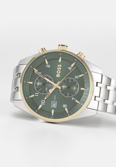 Montre chronographe pour homme avec un cadran vert, un bracelet en acier inoxydable argenté, des accents dorés et deux sous-cadrans. Affichage de la date à la position 6 heures.