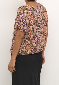 Blouse fleurie en rose, orange et vert avec des manches courtes. Coupe ample et tissu texturé, présentant un motif réparti sur toute la surface.