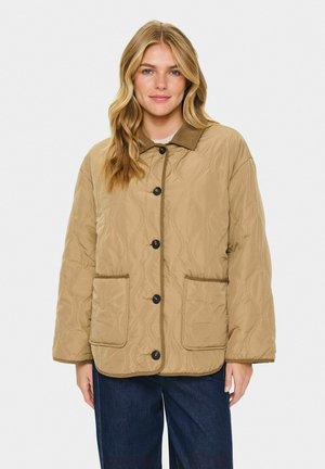 Gequilted beige jas met een kraag, knoopsluiting en twee voorkennis. Bevat een gestructureerd oppervlak en contrasterende afwerking.