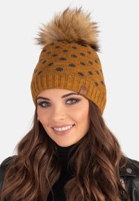 Knit mustard-yellow beanie with black polka dots, featuring a fluffy fur pom-pom on top and a ribbed cuff. Textured, warm material.