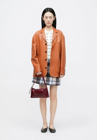 Blazer de couro castanho, camisa branca com padrão, saia mini de xadrez, bolsa bordô, sapatos pretos; apresenta texturas e cores variadas.