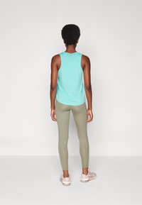 Top sin mangas de color azul claro, leggings verdes y zapatillas deportivas de color rosa pálido. Tejido suave, diseño ajustado y estilo minimalista.