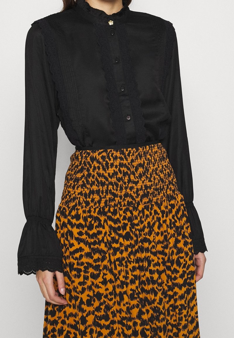 Femme portant un haut noir à manches longues avec des détails en dentelle et une jupe imprimée léopard orange et noir avec une taille froncée.