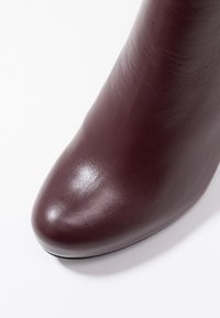 Burgundy leather ankle boot with a rounded toe, smooth texture, and subtle sheen. No visible hardware or patterns. Minimalist design.