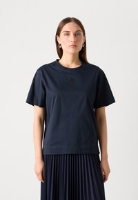 Navy short-sleeve cotton t-shirt with a round neckline and embroidered logo on the chest, paired with a pleated skirt.