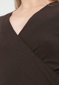 Top marrone in tessuto a coste con scollo profondo a V e design a incrocio, che mette in risalto la texture e le pieghe strutturate.