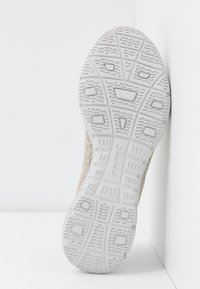 Suela de zapato con una parte inferior de goma blanca texturizada que presenta un patrón de agarre, y que se transforma en un material de malla superior beige. Logo visible.