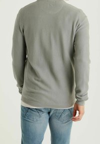 Vaffelstickad långärmad skjorta i ljusgrått, med ribbade ärmmuddar och rundad nederkant. Matchad med ljusblå jeans.