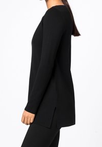 Tunique noire à manches longues avec fentes sur les côtés, fabriquée dans un tissu doux. Dotée d'un col rond et d'une silhouette légèrement surdimensionnée.