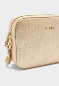 Geantă din piele texturată bej cu logo embosat, accesorii din aur și închidere cu fermoar. Are o curea detasabilă și o formă rectangulară elegantă.
