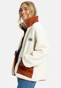 Witte fleece jas met een bruine nylon kraag, voorzien van een logo patch en zijzakken. Textuurstof en relaxte pasvorm.
