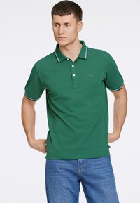 Zielona koszulka polo z kołnierzykiem, z guzikiem na dwa guziki i kontrastowym paskiem na kołnierzu i rękawach, wykonana z tkaniny bawełnianej.